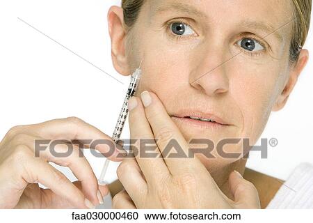 Stock Image - Woman giving herself botox injection, close-up. Fotosearch