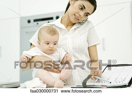 Woman holding baby, using cell phone and looking at agenda View Large Photo Image Stock Image - Woman holding baby, using cell phone and looking at agenda. Fotosearch