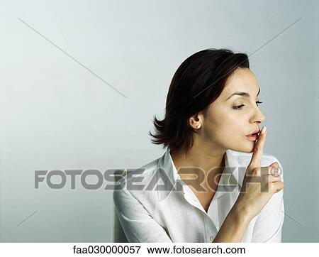 Stock Photo - Woman holding finger over lips, looking away. Fotosearch