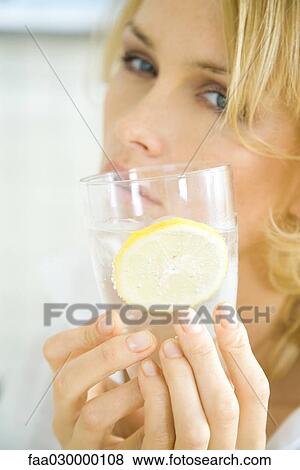 Stock Photo - Woman holding glass of sparkling water with lemon slice. Fotosearch