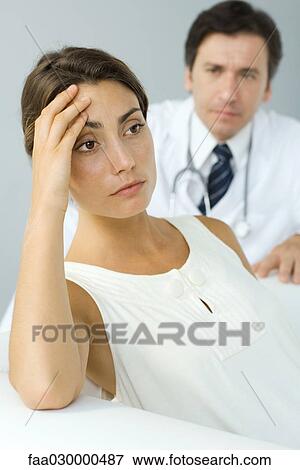 Woman holding head, looking away, doctor in background View Large Photo Image Stock Photo - Woman holding head, looking away, doctor in background. Fotosearch