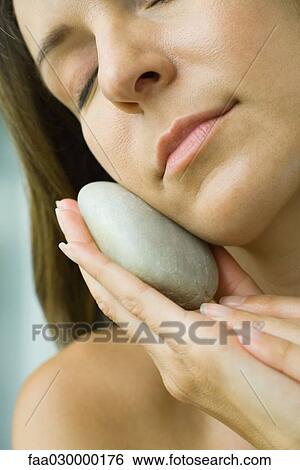 Stock Photograph - Woman holding smooth stone against face, cropped. Fotosearch