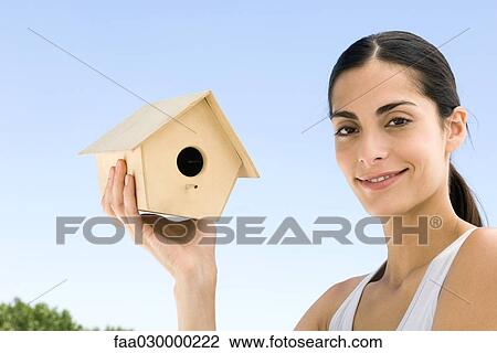 Stock Image - Woman holding up birdhouse, smiling at camera. Fotosearch