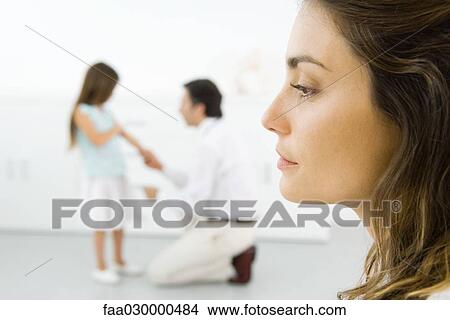 Woman looking away, profile, doctor examining girl in background View Large Photo Image Picture - Woman looking away, profile, doctor examining girl in background. Fotosearch
