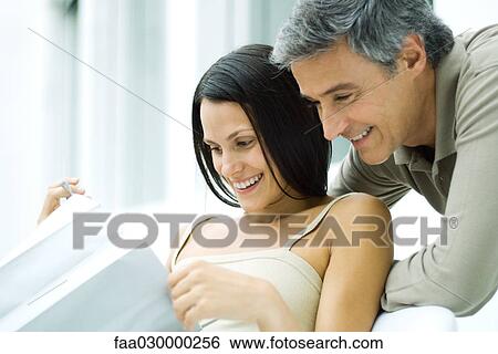 Woman opening gift bag, man looking over her shoulder, both smiling View Large Photo Image Stock Photograph - Woman opening gift bag, man looking over her shoulder, both smiling. Fotosearch