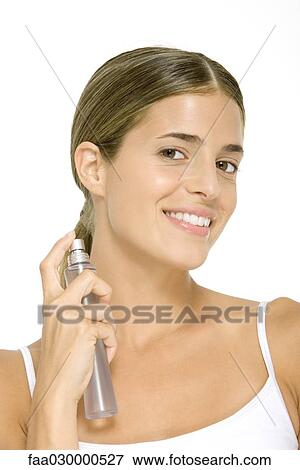 Stock Photo - Woman putting on perfume, smiling at camera. Fotosearch