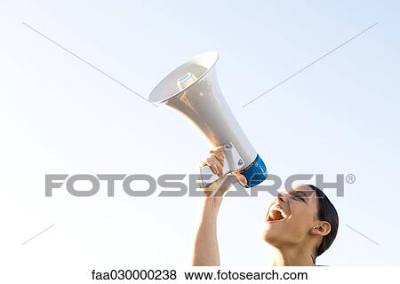 Stock Photo - Woman shouting into megaphone, low angle view, cropped. Fotosearch