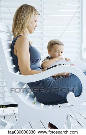 Stock Image - Woman sitting in rocking chair, looking at book with young son. Fotosearch
