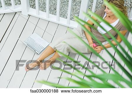 Woman sitting on deck, laptop nearby, high angle view View Large Photo Image Stock Photo - Woman sitting on deck, laptop nearby, high angle view. Fotosearch