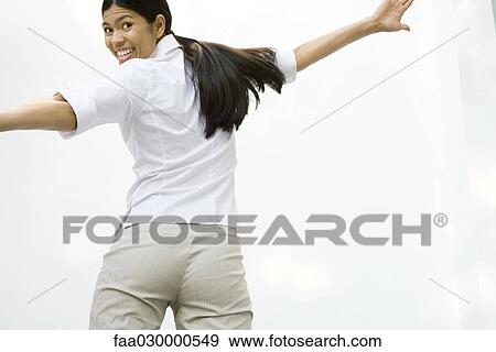 Woman smiling over shoulder at camera, arms spread, rear view View Large Photo Image Stock Photo - Woman smiling over shoulder at camera, arms spread, rear view. Fotosearch