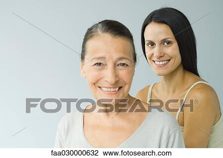 Woman standing behind senior woman, both smiling at camera, portrait View Large Photo Image Stock Image - Woman standing behind senior woman, both smiling at camera, portrait. Fotosearch