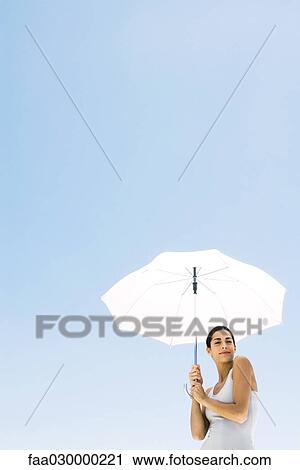 Woman standing under umbrella, smiling at camera, low angle view View Large Photo Image Stock Image - Woman standing under umbrella, smiling at camera, low angle view. Fotosearch