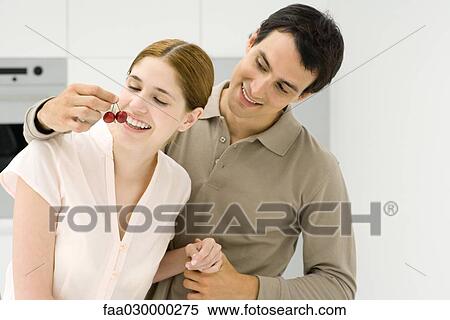 Young couple in kitchen, man holding cherries in front of woman's mouth View Large Photo Image Stock Photography - Young couple in kitchen, man holding cherries in front of woman's mouth. Fotosearch