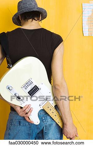 Young man holding electric guitar behind back, rear view View Large Photo Image Stock Image - Young man holding electric guitar behind back, rear view. Fotosearch