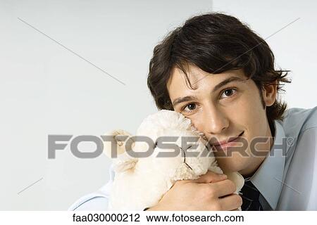 Young man holding stuffed toy against cheek, smiling at camera View Large Photo Image Stock Image - Young man holding stuffed toy against cheek, smiling at camera. Fotosearch