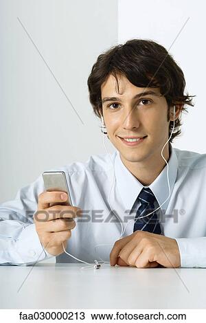 Young man listening to MP3 player, smiling at camera View Large Photo Image Stock Image - Young man listening to MP3 player, smiling at camera. Fotosearch