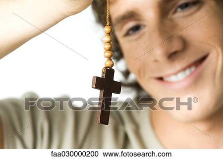 Stock Image - Young man looking at cross, smiling, close-up. Fotosearch
