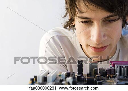 Young man looking down at computer motherboard, close-up View Large Photo Image Stock Image - Young man looking down at computer motherboard, close-up. Fotosearch