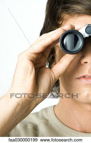 Stock Photo - Young man looking through binoculars, close-up, cropped. Fotosearch