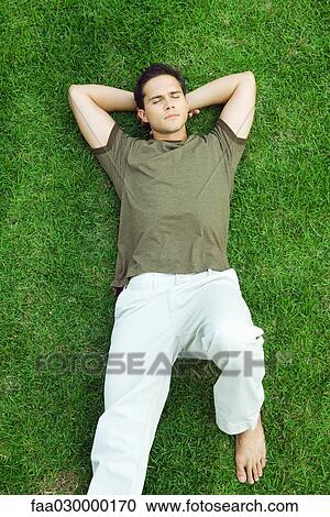 Young man lying on grass with eyes closed, high angle view View Large Photo Image Stock Image - Young man lying on grass with eyes closed, high angle view. Fotosearch