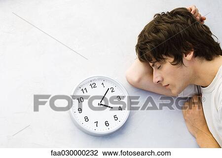 Young man lying on the ground next to clock, eyes closed View Large Photo Image Stock Image - Young man lying on the ground next to clock, eyes closed. Fotosearch