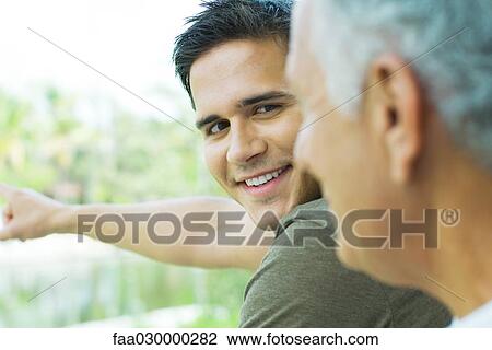 Young man pointing, looking over shoulder at father, cropped view View Large Photo Image Stock Image - Young man pointing, looking over shoulder at father, cropped view. Fotosearch