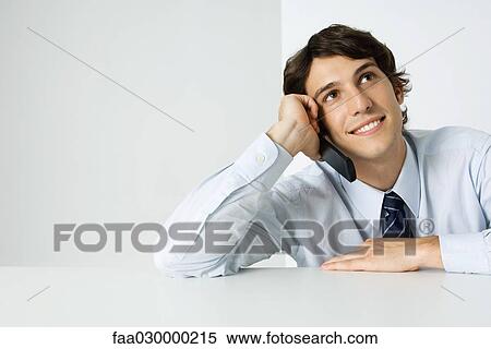 Young man using cell phone, looking up, smiling View Large Photo Image Stock Photography - Young man using cell phone, looking up, smiling. Fotosearch