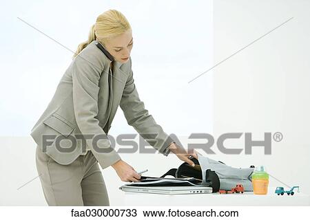 Stock Image - Young professional mother preparing bag while using cell phone. Fotosearch