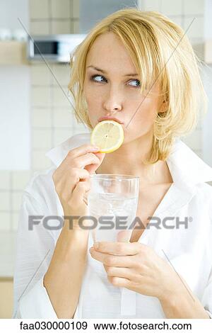 Young woman biting into a slice of lemon, looking away, holding a glass of water View Large Photo Image Stock Photo - Young woman biting into a slice of lemon, looking away, holding a glass of water. Fotosearch