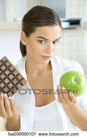 Young woman holding apple in one hand and large bar of chocolate in the other View Large Photo Image Stock Photo - Young woman holding apple in one hand and large bar of chocolate in the other. Fotosearch
