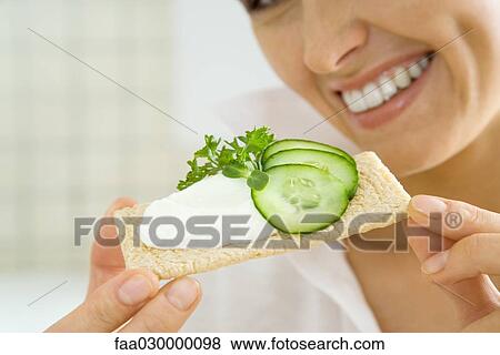 Young woman holding up cracker topped with cucumbers and cheese spread, cropped View Large Photo Image Stock Photo - Young woman holding up cracker topped with cucumbers and cheese spread, cropped. Fotosearch