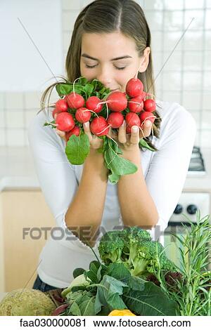 Young woman in kitchen with an assortment of vegetables, smelling bunch of radishes View Large Photo Image Stock Image - Young woman in kitchen with an assortment of vegetables, smelling bunch of radishes. Fotosearch