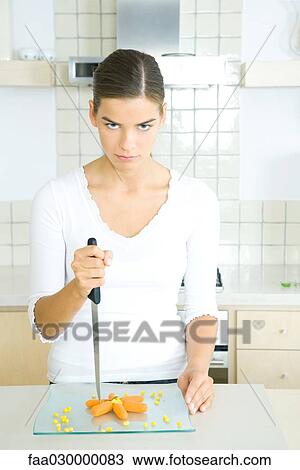 Young woman in kitchen with plate of carrot sticks, holding knife menacingly View Large Photo Image Stock Image - Young woman in kitchen with plate of carrot sticks, holding knife menacingly. Fotosearch