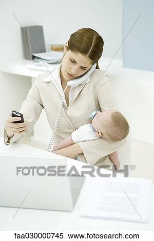 Young working mother holding baby, talking on landline phone and looking at cell phone View Large Photo Image Stock Photography - Young working mother holding baby, talking on landline phone and looking at cell phone. Fotosearch