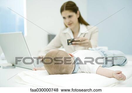 Young working mother making credit card purchase, baby lying on desk, focus on baby in foreground View Large Photo Image Stock Photo - Young working mother making credit card purchase, baby lying on desk, focus on baby in foreground. Fotosearch