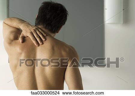 Picture - Bare-chested man touching his back, rear view. Fotosearch