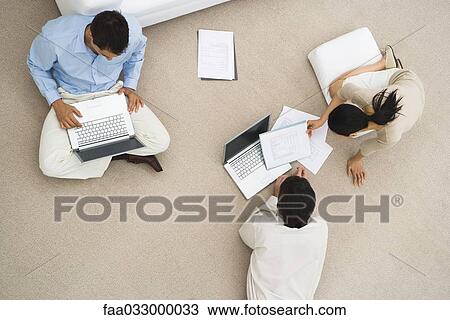 Stock Image - Business associates sitting together on floor, using laptop computers, overhead view. Fotosearch