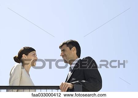 Business associates standing outdoors, smiling at each other, low angle view View Large Photo Image Stock Image - Business associates standing outdoors, smiling at each other, low angle view. Fotosearch