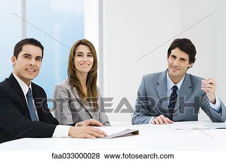 Stock Photo - Business colleagues sitting at table, smiling at camera. Fotosearch