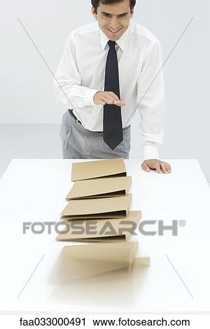 Stock Image - Businessman knocking over binders, smiling at camera. Fotosearch