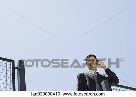 Businessman using cell phone outdoors, smiling at camera, low angle view View Large Photo Image Stock Image - Businessman using cell phone outdoors, smiling at camera, low angle view. Fotosearch