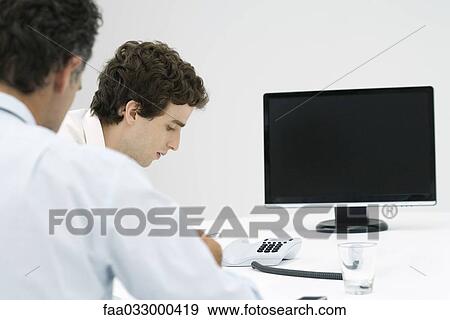 Stock Photo - Businessmen listening to conference call, over the shoulder view. Fotosearch