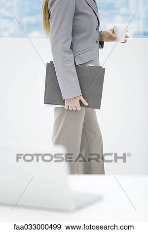 Businesswoman holding disposable coffee cup and folders, side view, cropped View Large Photo Image Stock Photo - Businesswoman holding disposable coffee cup and folders, side view, cropped. Fotosearch