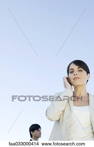 Picture - Businesswoman using cell phone, smiling at camera, low angle view. Fotosearch