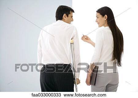Stock Image - Colleagues standing side by side, chatting, one using crutches. Fotosearch