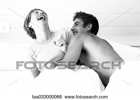 Stock Photograph - Couple in bed, both laughing. Fotosearch
