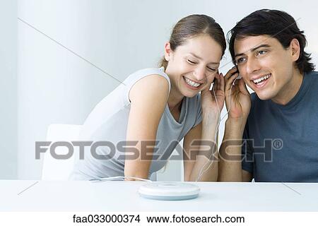 Couple listening to CD player together, sharing earphones, smiling View Large Photo Image Picture - Couple listening to CD player together, sharing earphones, smiling. Fotosearch