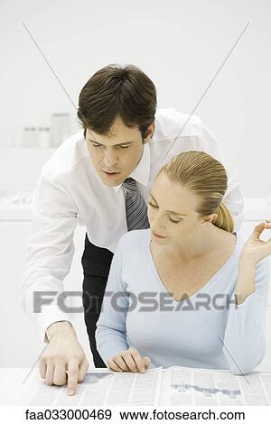Stock Photo - Couple reading newspaper together, man looking over woman's shoulder. Fotosearch