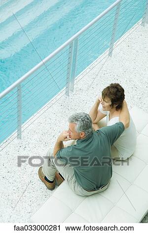 Stock Image - Couple sitting together on balcony, looking at the view, high angle view. Fotosearch