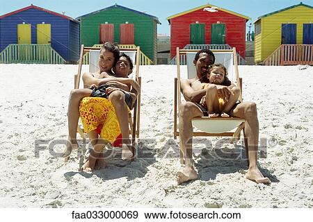 Stock Photo - Family at the beach, parents sitting in deckchairs and holding children on their laps. Fotosearch